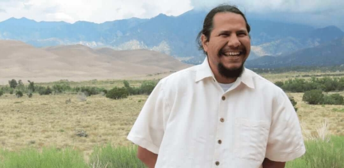 Organizer Noe Orgaz smiles in front of Sand Dunes at Great Sand Dunes National Park.