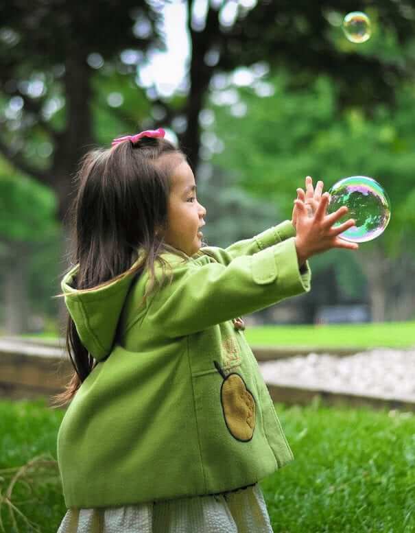 A kid in a green jacket catches bubbles