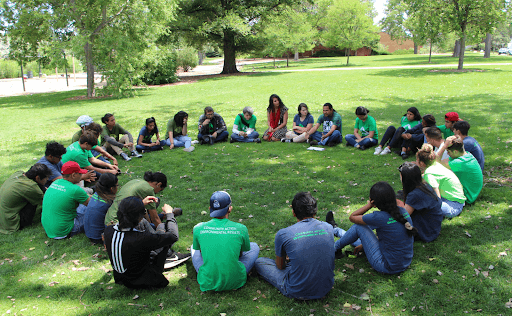 Youth Promotores sit in a circle in the grass
