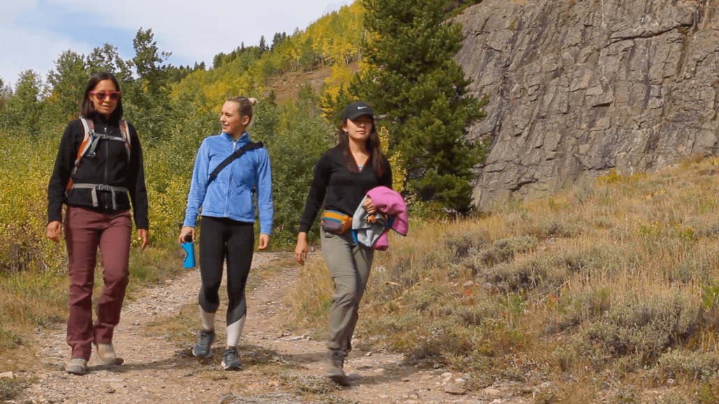 Three women walk on a trail at Camp Hale