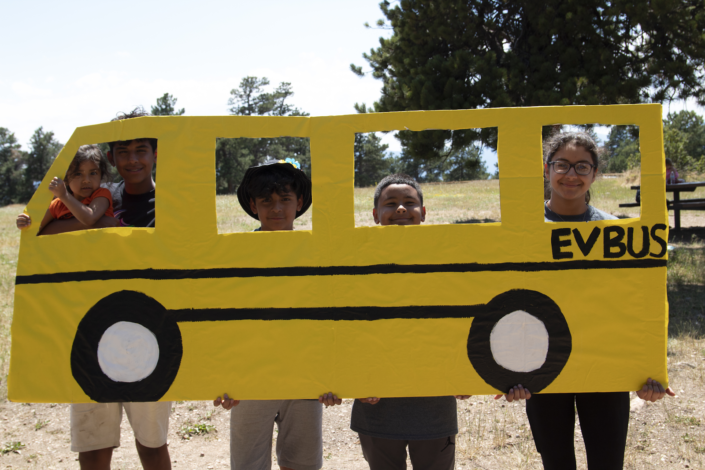Five kids peer out of a cutout cardboard bus.