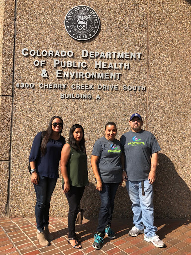 Four people stand in front of the Colorado Department of Public Health and Environment Building