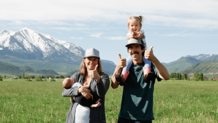 Family of four stands in a field in front of a mountain