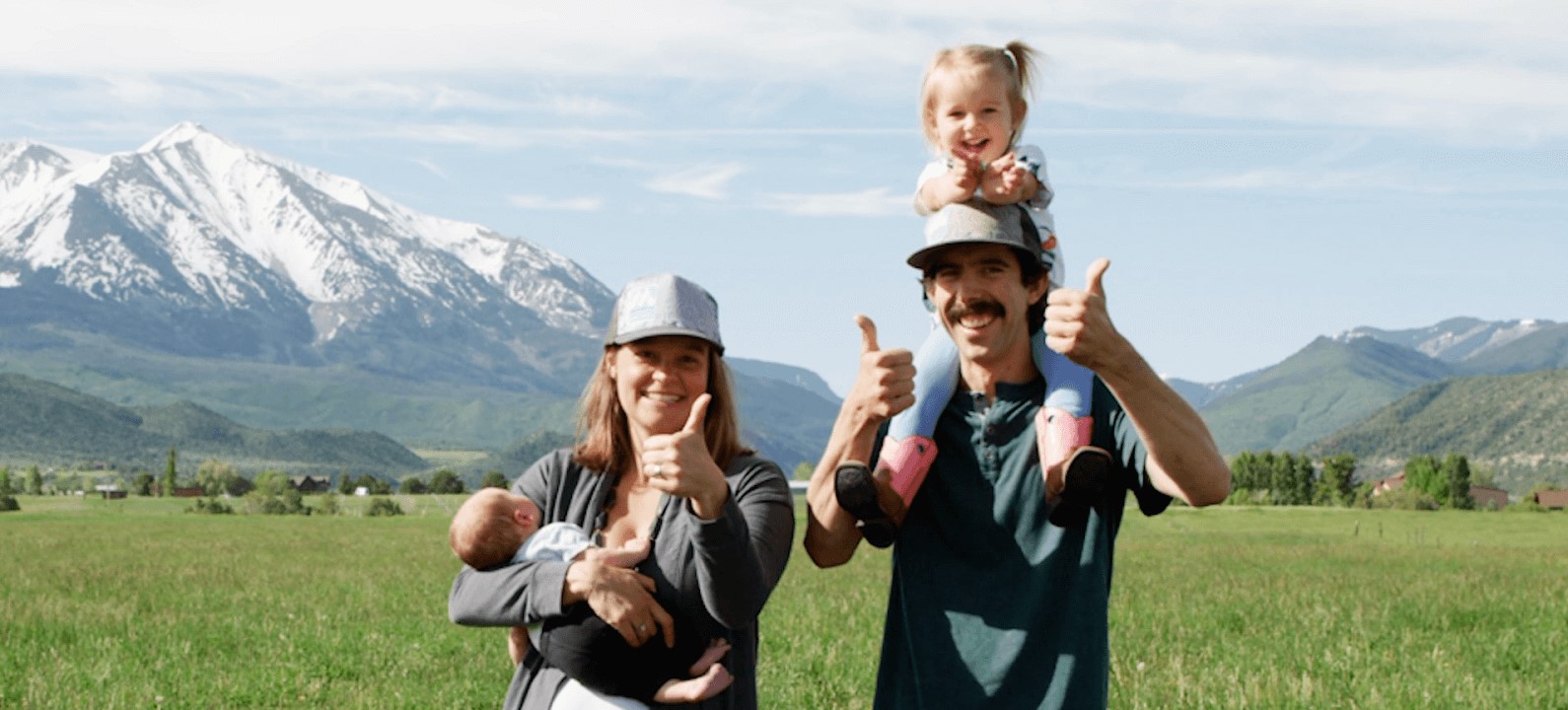 Family of four stands in grass in front of a mountain, advocating for iconic winters